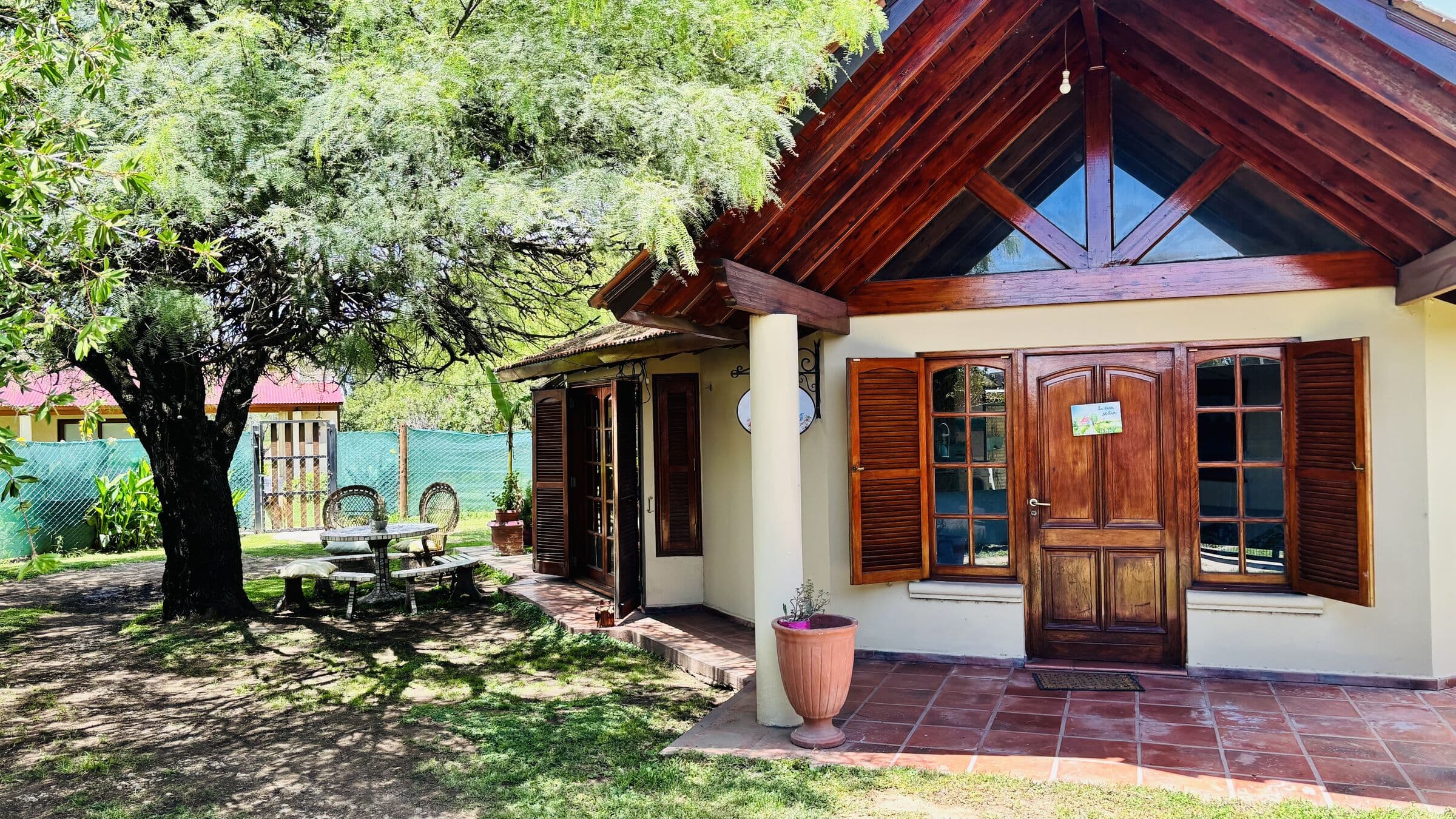 La casa vista desde el jardín, con el algarrobo y una mesa a la sombra