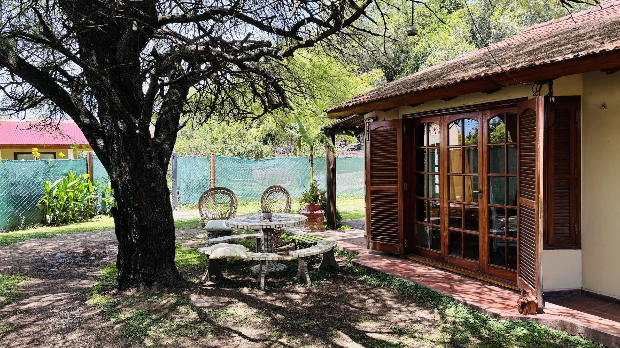 Galería con puertas ventana de madera y mesa de mosaico bajo el algarrobo