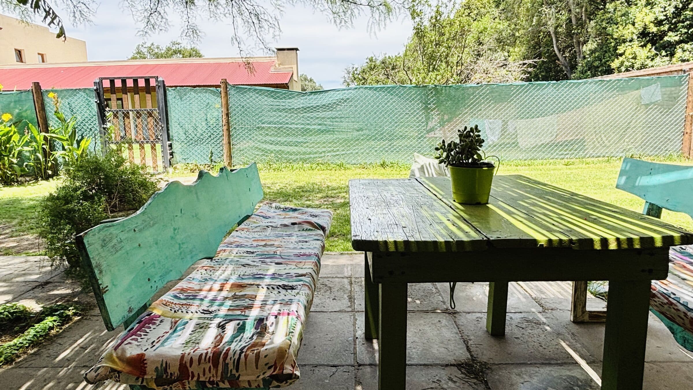 Banco turquesa con almohadón estampado y mesa verde en el patio
