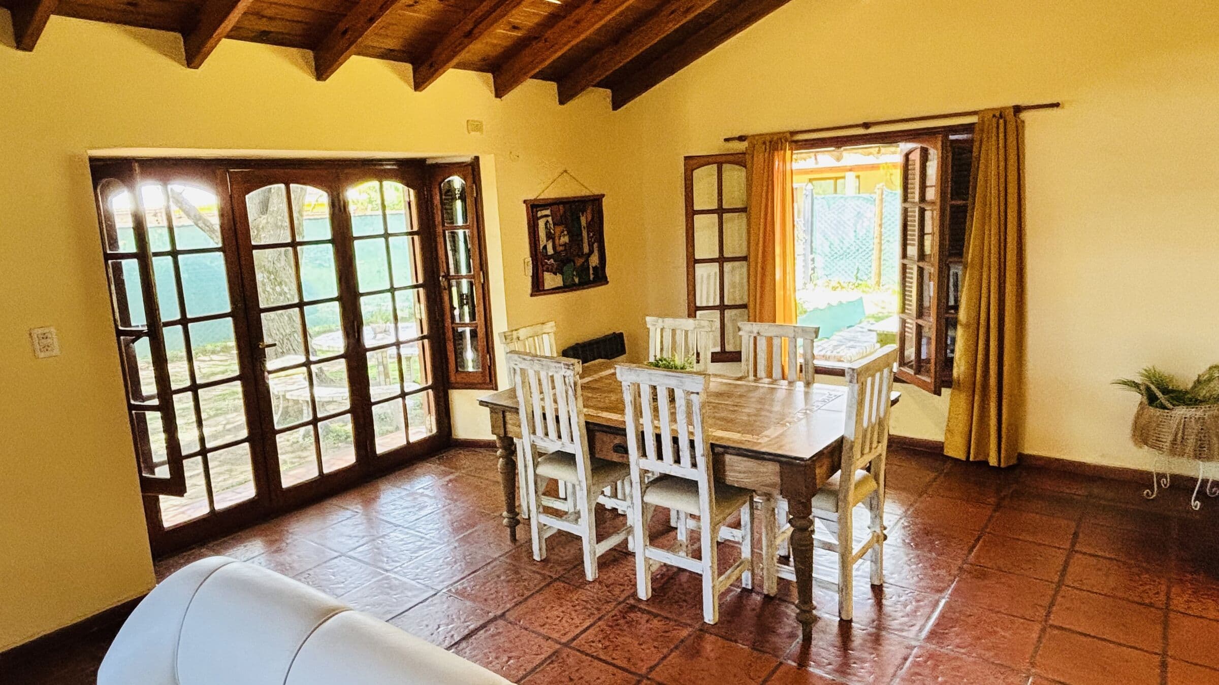Comedor con mesa de madera, sillas blancas y puertas abiertas al jardín